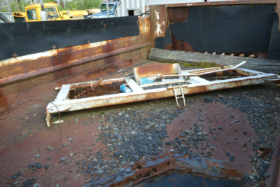 Dump truck bed showing rusted metal and a damaged metal frame lying inside the bed with gravel and debris.