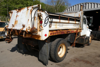 Rear/side view of a white International dump truck with a rusted dump bed. Visible text includes 'International' emblem on cab side. No clear model numbers readable.