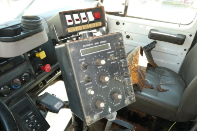 Dashboard panel with multiple switches and gauges inside an International 4900 dump truck cab; visible wear, control panel labeled 'Pennant 2000 Series' with knobs, buttons and a few warning lights.
