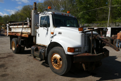 International 4900 dump truck showing front view with white cab, orange marker lights, and rusted wheels.