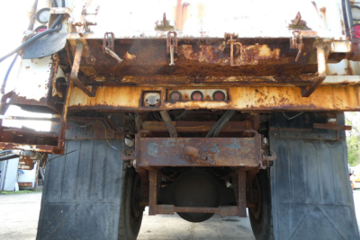 Dump truck rear view showing rusty chassis and differential, underside of cargo bed with hitch hooks and frame members.