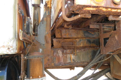 Heavy rust on the undercarriage of a dump truck showing frame rails, brackets, and hydraulic components.