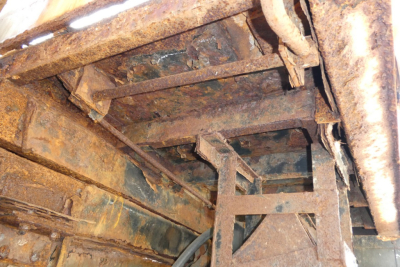 Underbody of a dump truck showing rusted frame and structural supports.