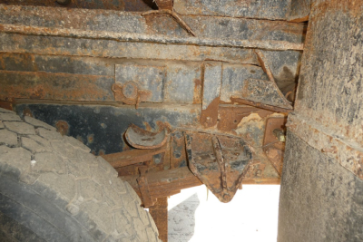 Truck undercarriage view showing suspension components and frame with dirt and rust, wheel and leaf springs visible.
