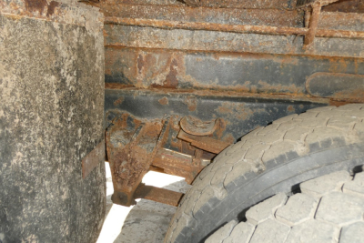 Dump truck undercarriage showing rusted frame rails and wheel with heavy wear.