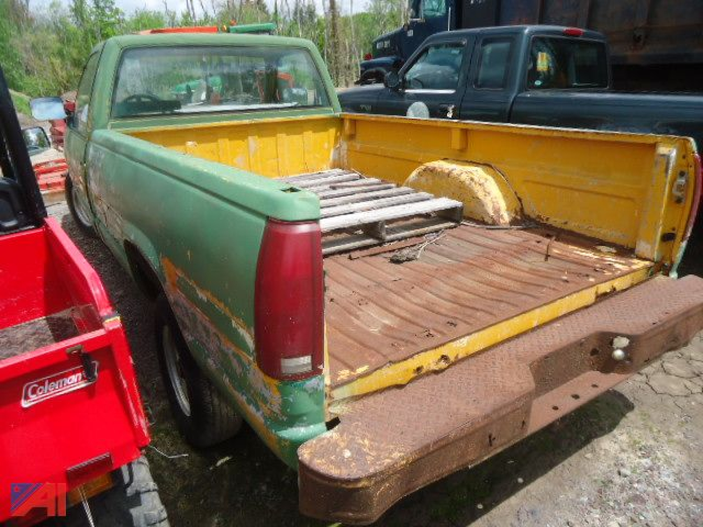 1981-1991 Chevrolet C/K pickup truck bed and rear quarter with green paint and yellow bed, visible rust and barn red tail light lens.