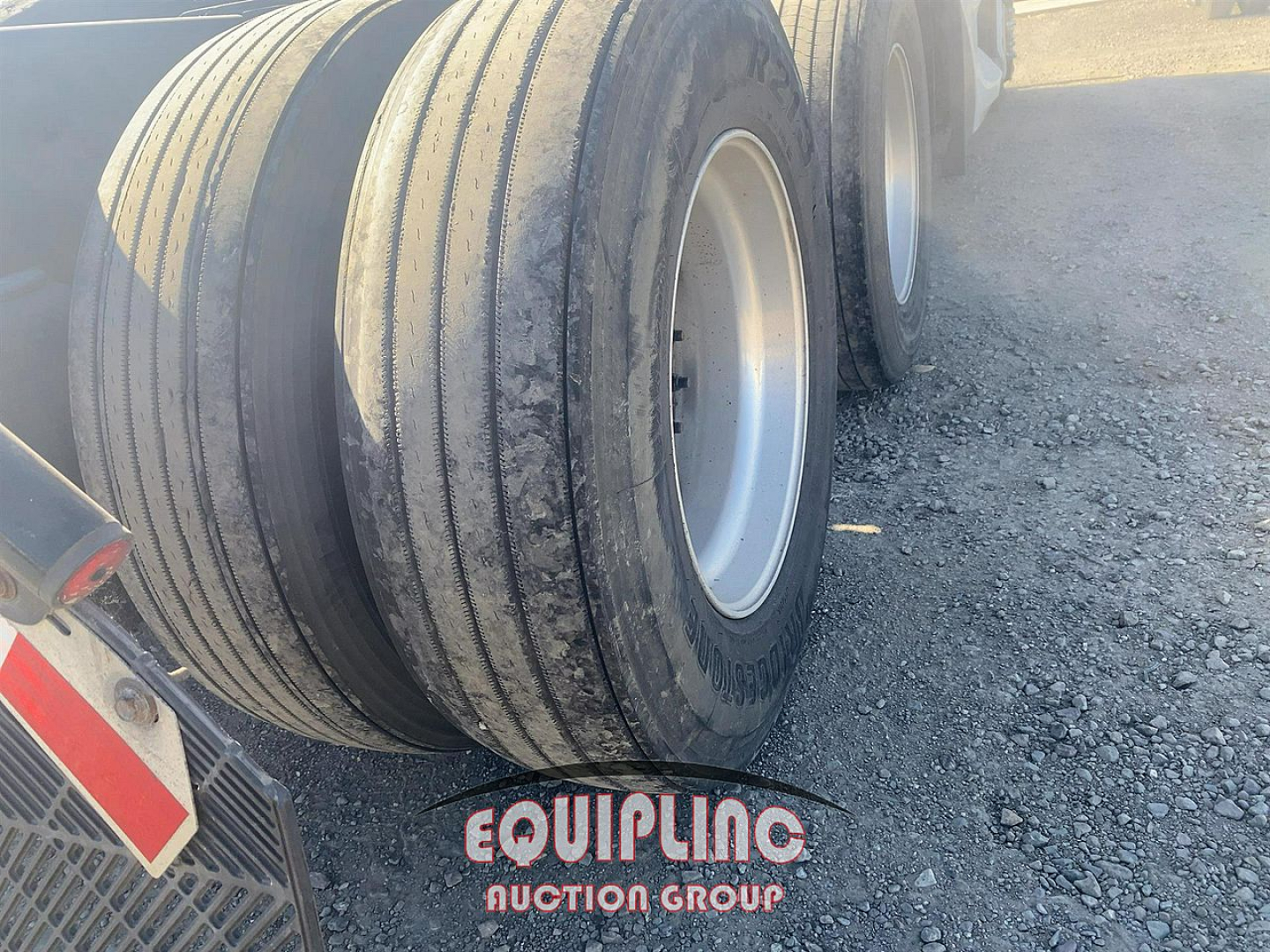 Trailer wheels and tires with Equipping Auction Group logo on the ground near wheel wells; no vehicle badge visible.