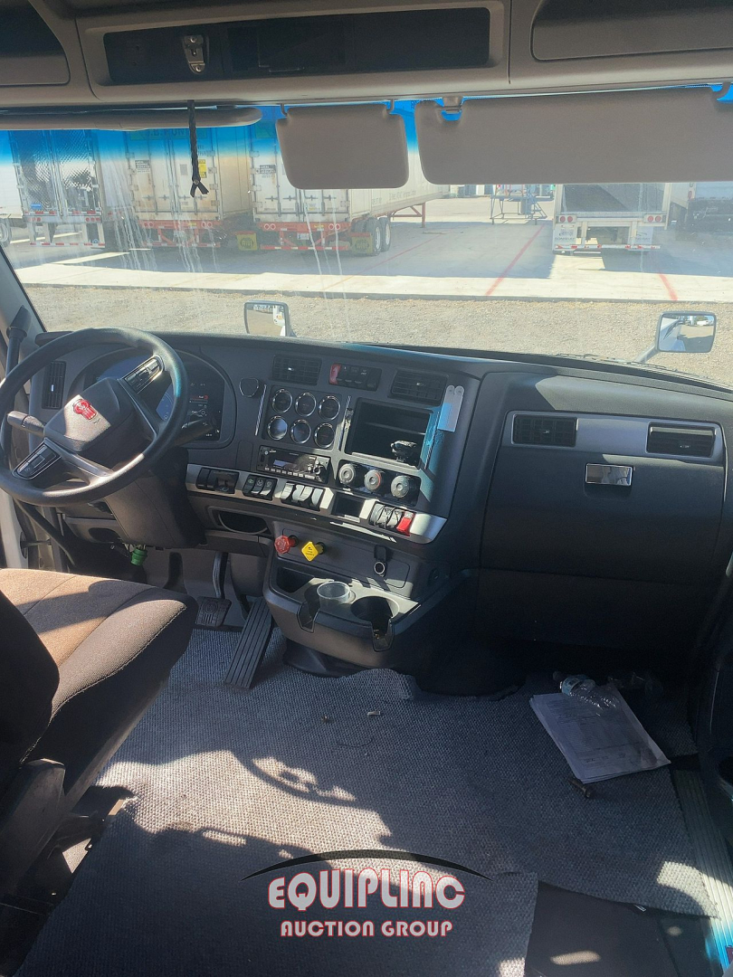 Kenworth T680 truck cockpit showing steering wheel, dashboard gauges, center console with control switches, and sun visors.