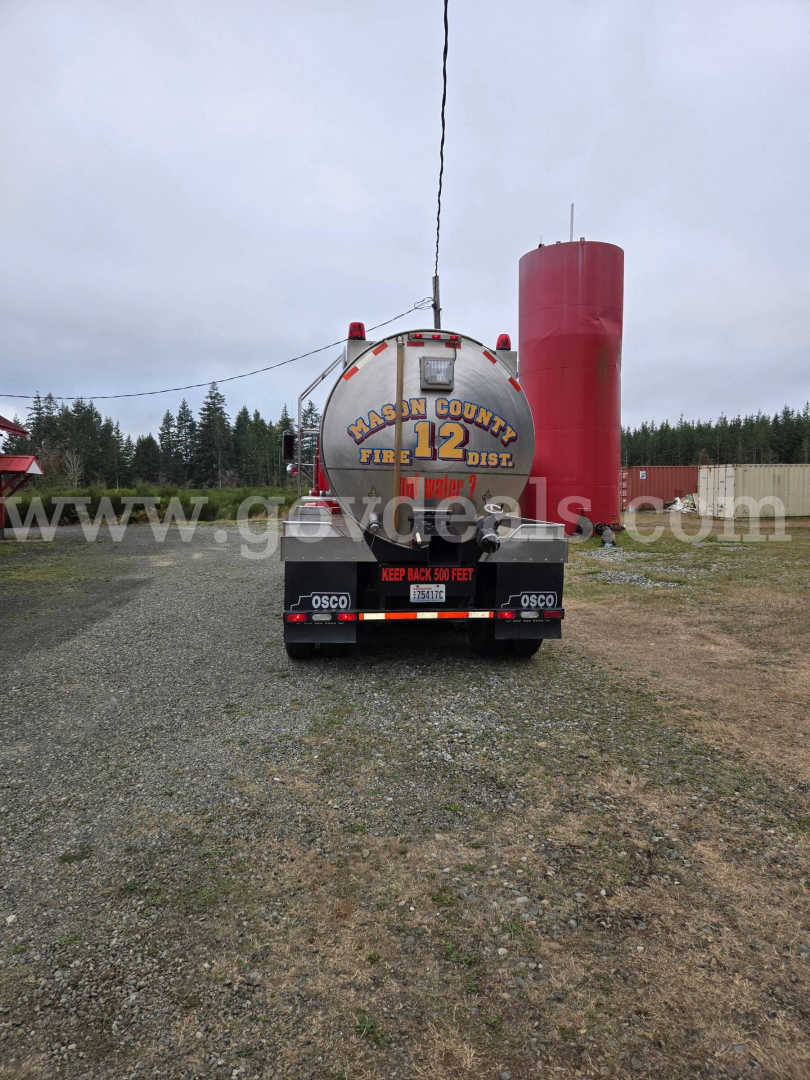Tank trailer viewed from rear showing large cylindrical tank with red cap on right, bumper label ‘Keep Back 50 Feet’ and tanker rear with hazard markings. Freightliner-style trailer with water tank markings.