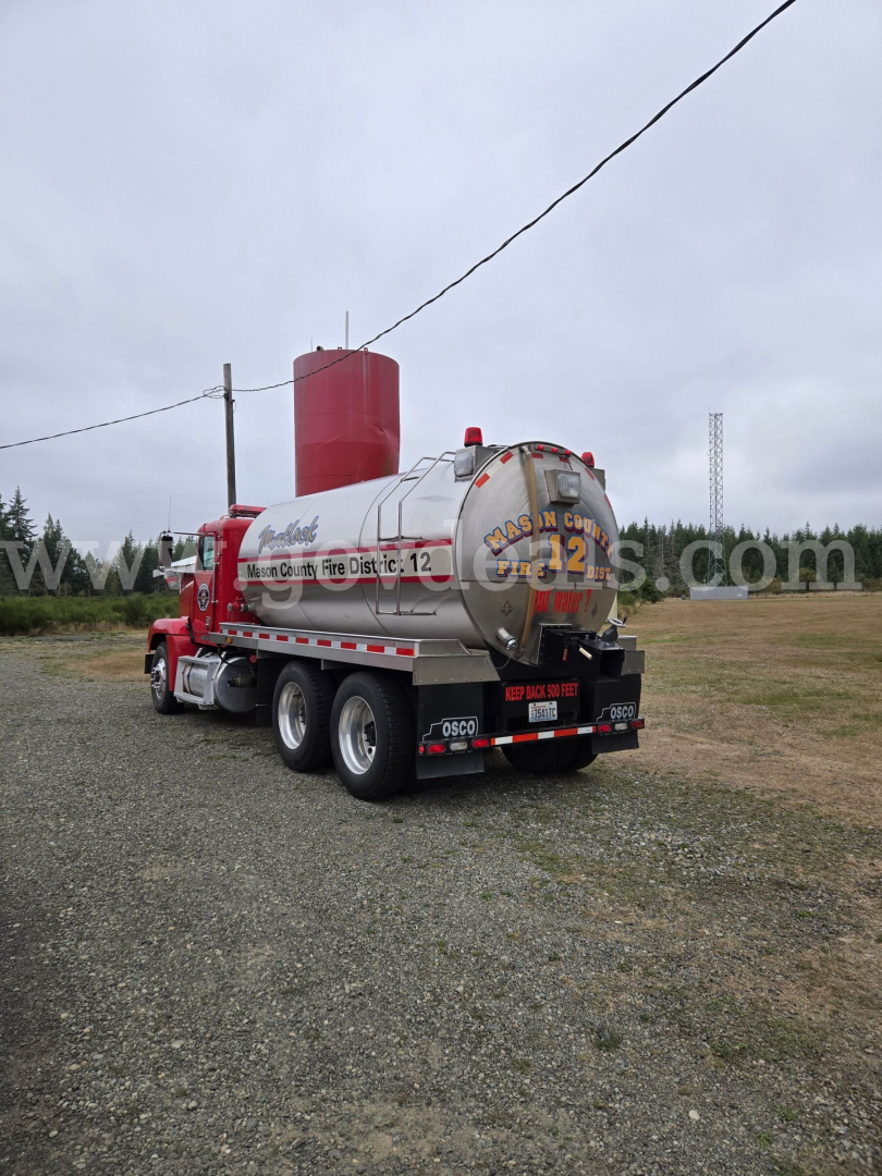 Tank truck rear three-quarter view showing stainless tank and red cab on Freightliner FLD120 with tanker lettering and safety decals.