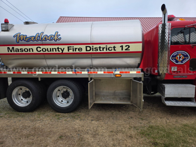 Tank truck side showing 'Mackblock' or 'Madblock' style logo, 'Mason County Fire District 12' on tank, three-axle rear wheels, toolbox under tank, red cab with district badge, and website watermark 'govde...'