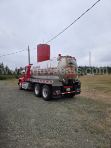 Tank truck rear three-quarter view showing stainless tank and red cab on Freightliner FLD120 with tanker lettering and safety decals.