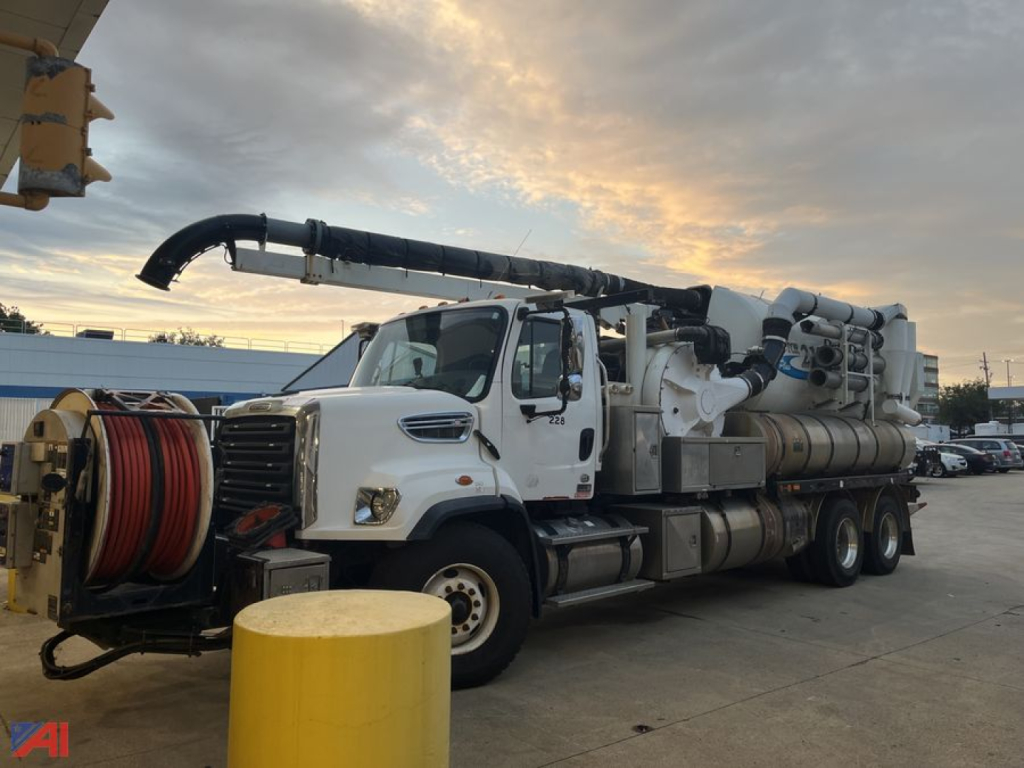 Freightliner 108SD Vactor truck in service bay showing vacuum hose reel and large rear vacuum system with multiple tanks and piping.