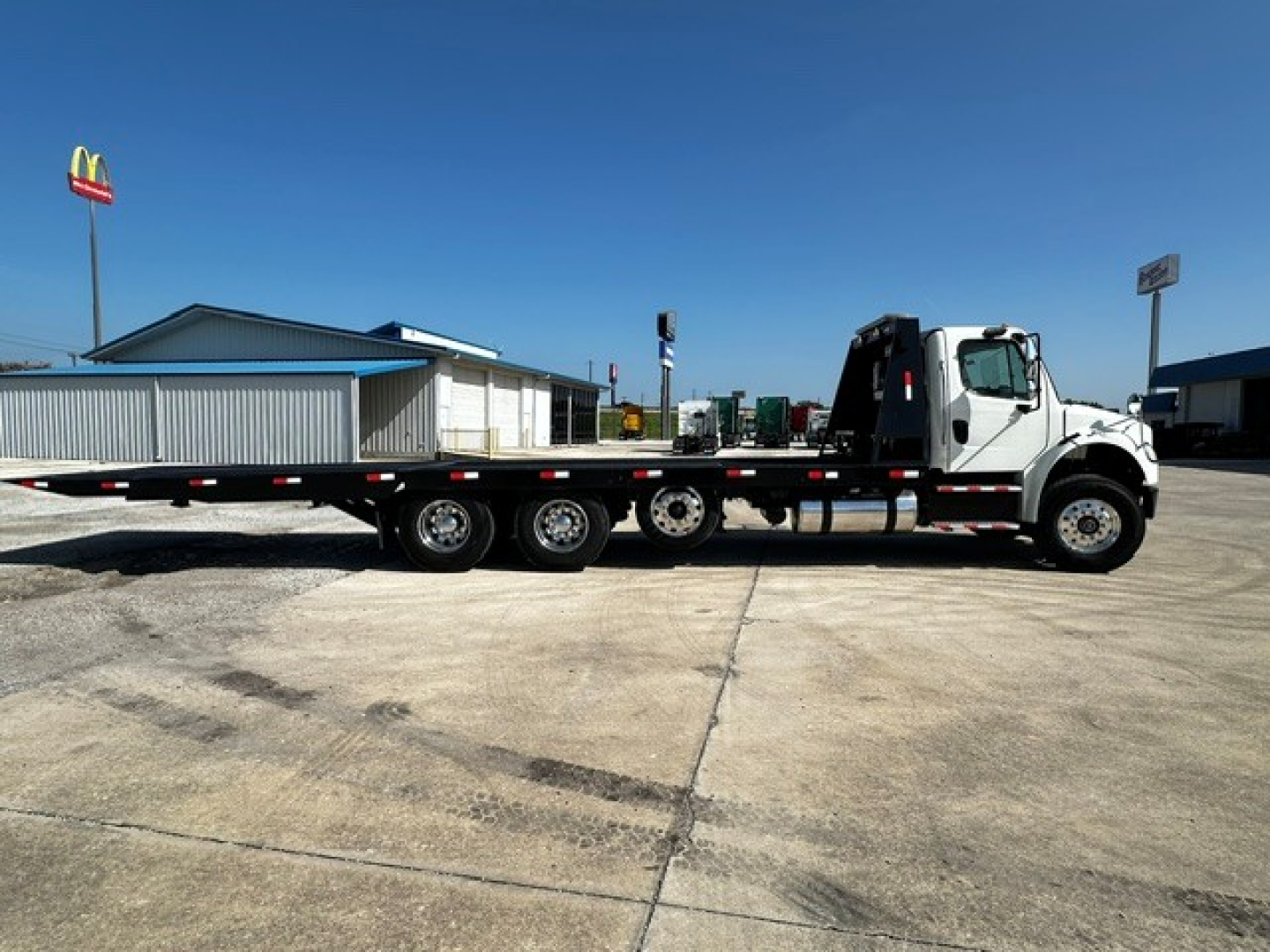 2018 Freightliner M2106 rollback truck with long flatbed and wheelset configuration, visible branding and equipment in lot.