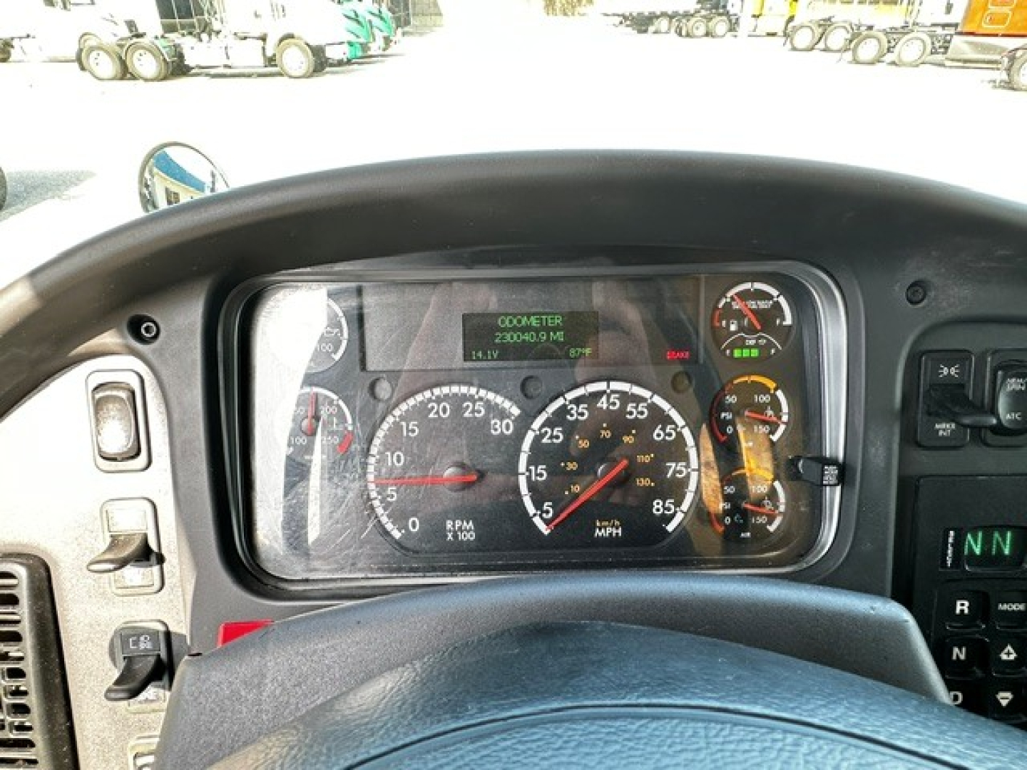 Dashboard of a 2018 Freightliner M2106 cab showing analog gauges and digital monitor in center; steering wheel partially visible and truck interior front panel.