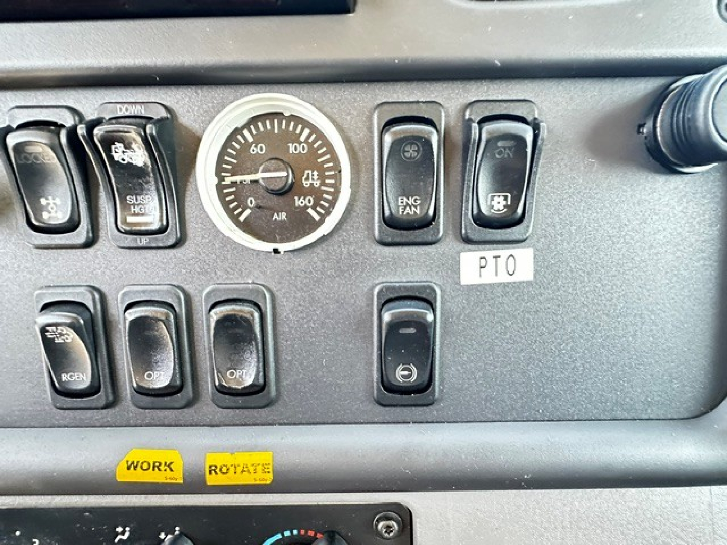 Dashboard control panel of a Freightliner truck showing gauges and switches. Visible text includes: a round gauge with numbers, various rocker switches labeled ENG FAN, OFF, ON, PTO, a small label 'PTO', and two yellow stickers reading 'WOR