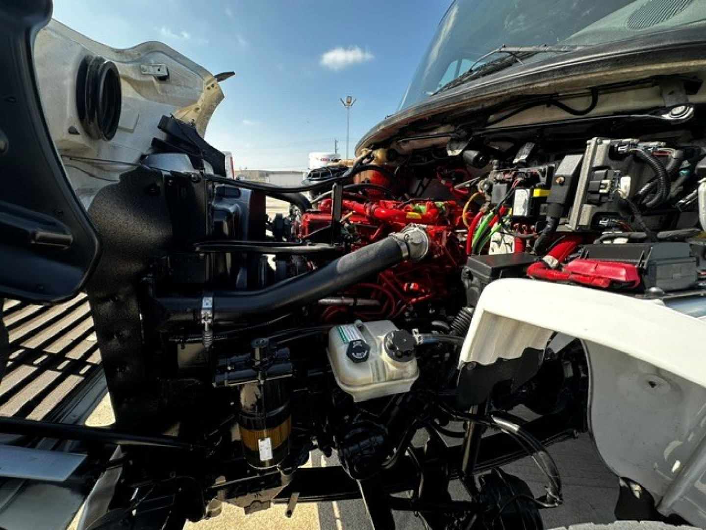 Front engine bay of a Freightliner M2106 rollback truck showing red engine components, black hoses, and white body panels.