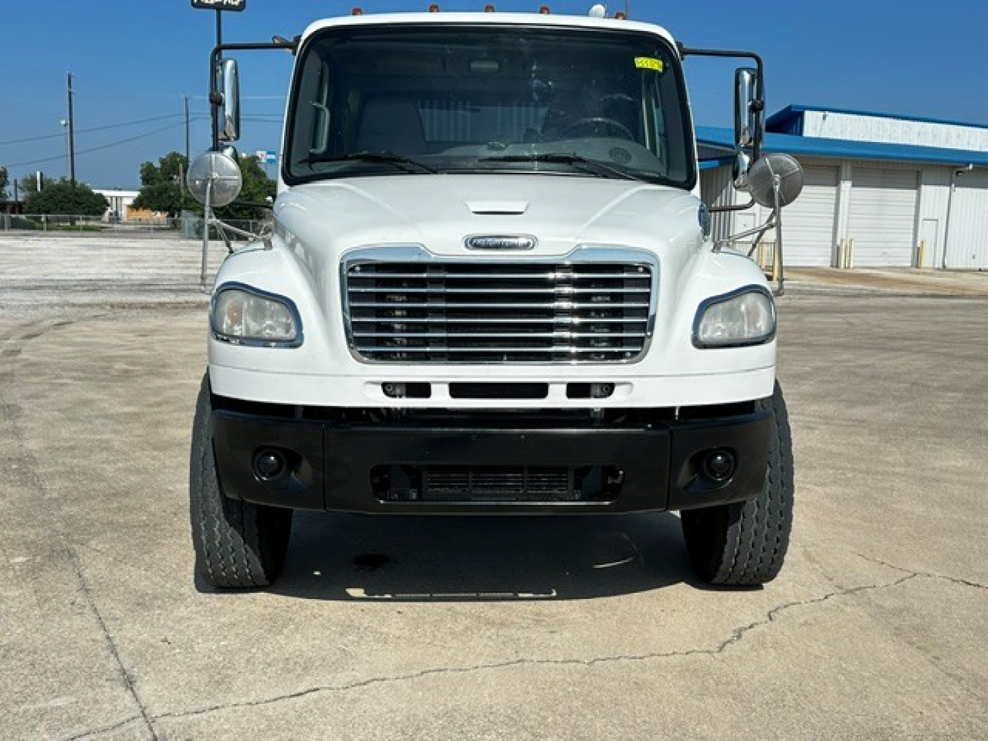 Front view of a white Freightliner M2106 rollback truck showing grille, bumper, headlights, and side mirrors.