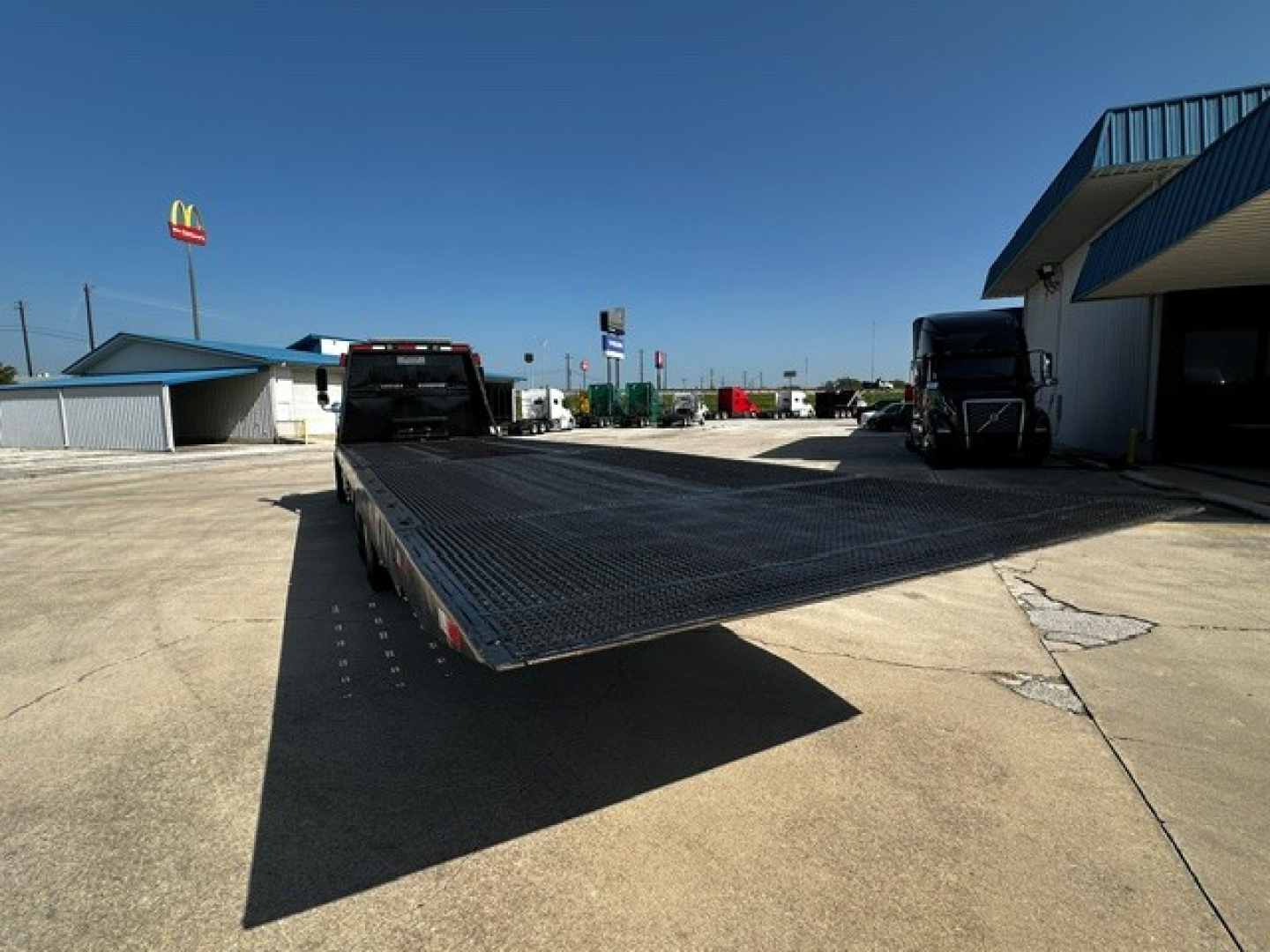 2018 Freightliner M2106 rollback truck with flatbed viewed from rear-left, showing long metallic deck and dual rear wheels