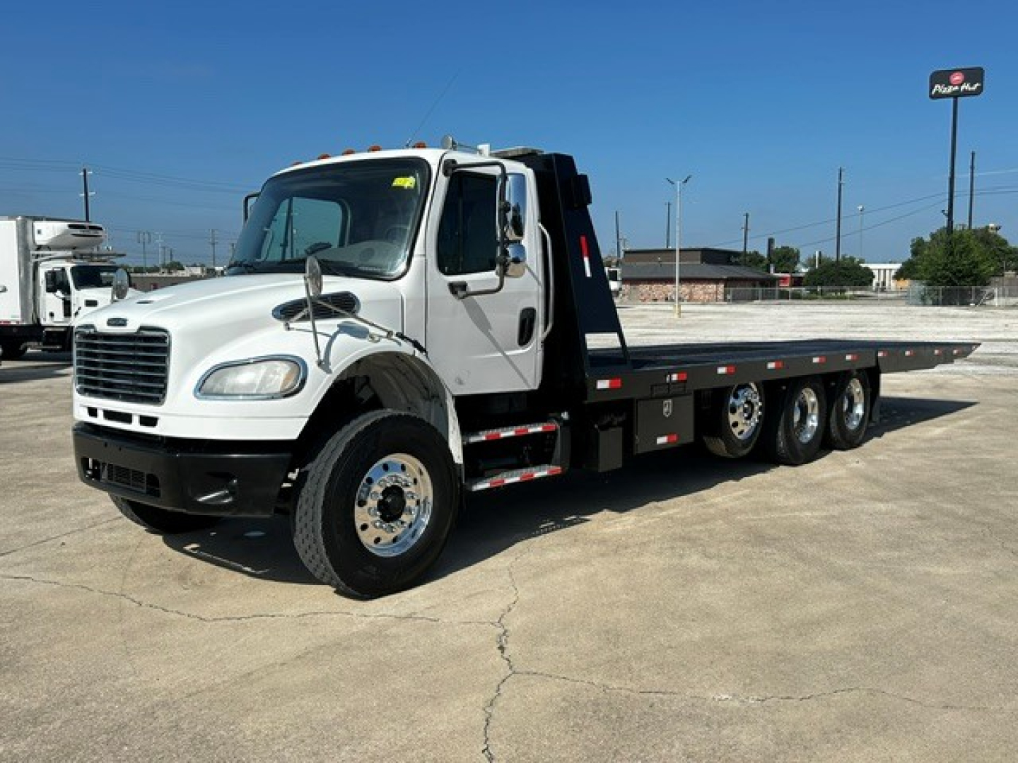 2018 Freightliner M2106 rollback truck shown from the front-left side with a long flatbed and hydraulic hooklift. visible text includes Freightliner-style grille and cab.