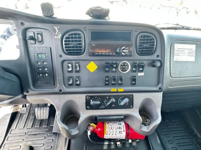 Dashboard of a Freightliner M2106 cab showing instrument panel, control switches, cup holders, and a fire extinguisher mounted under the dash.