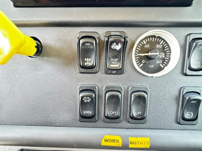 Dashboard panel of a 2018 Freightliner M2106 showing switches labeled LOCKED, SUSP HOT, and gauges; yellow ignition/handle visible on left; multiple rocker switches and a round gauge.