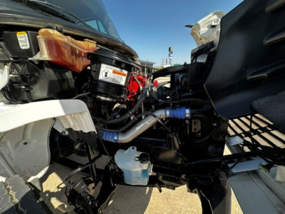 Freightliner M2106 engine bay showing exposed components, intake hoses, coolant reservoir, and various labels.
