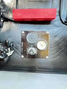 Trucks equipment panel showing pressure gauge and control knob in Freightliner M2106 salvage area, with red storage bin above. Visible label plate with gauge and knob.