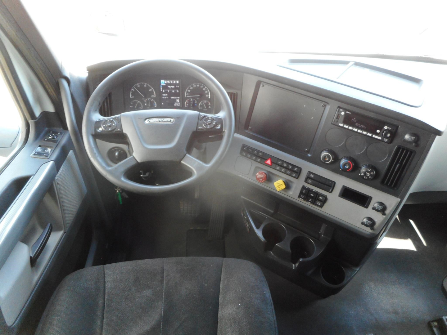 Cab interior of a Freightliner Cascadia 126 truck showing steering wheel, dashboard, and center console with display screens and control buttons.