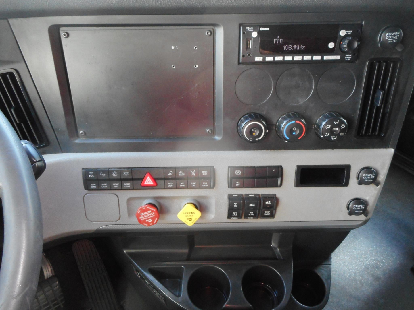 Dashboard view of a 2022 Freightliner Cascadia 126 sleeper cab showing radio, climate controls, warning switches, cup holders, and a large metal panel.