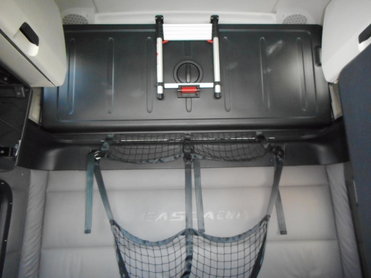 Truck interior cargo area of a 2022 Freightliner Cascadia 126 showing a storage bin, straps, and a net in the sleeper cab area.