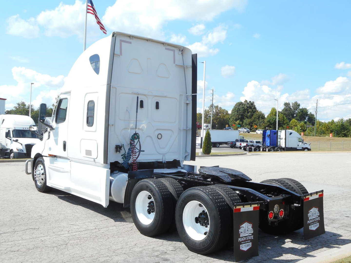 Freightliner Cascadia 126 sleeper tractor rear side view showing fifth wheel and dual rear axles with white cab and black chassis
