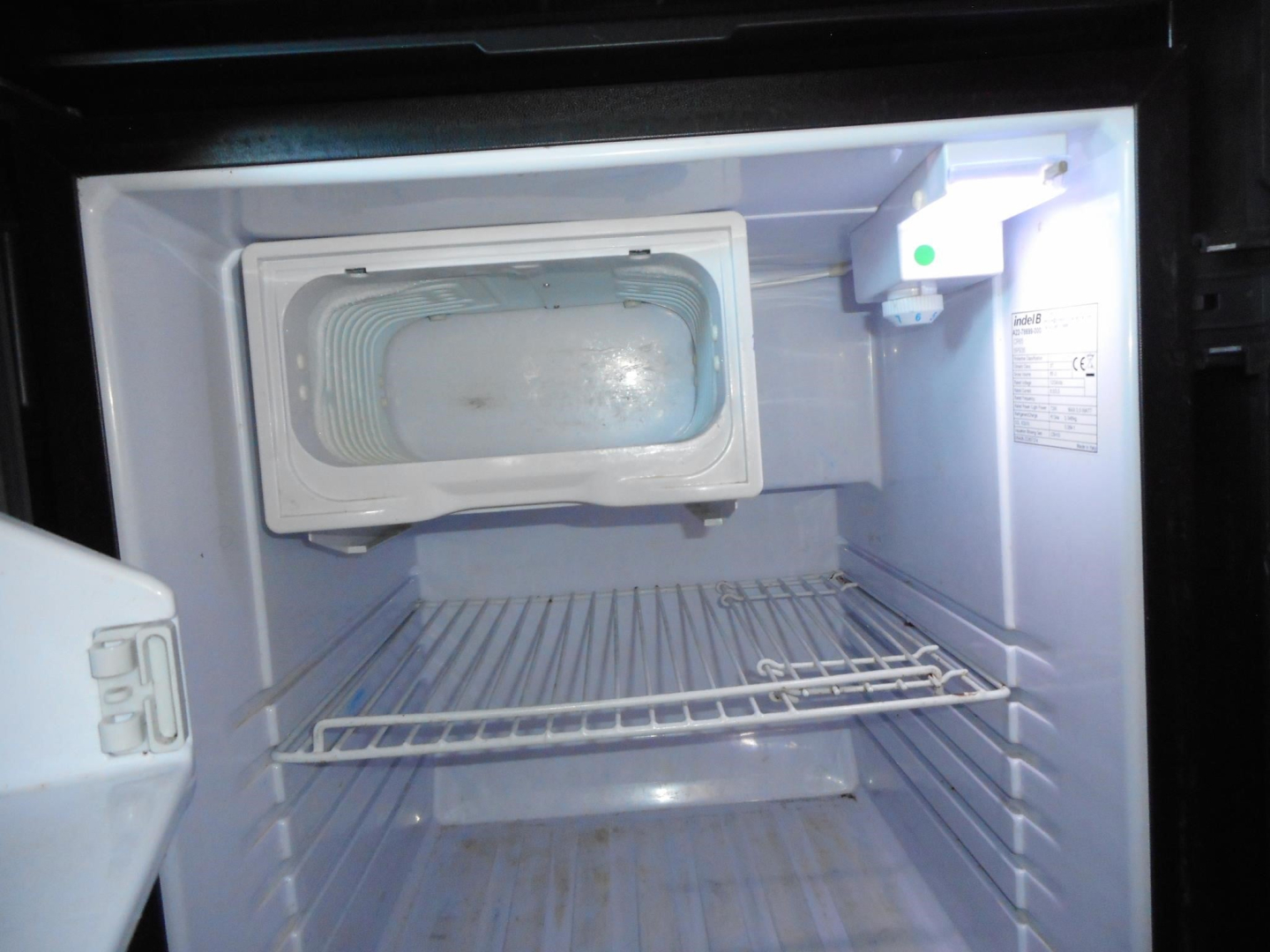Trunked image of a small refrigerator/freezer unit inside a Freightliner Cascadia sleeper cab with empty cargo area visible.