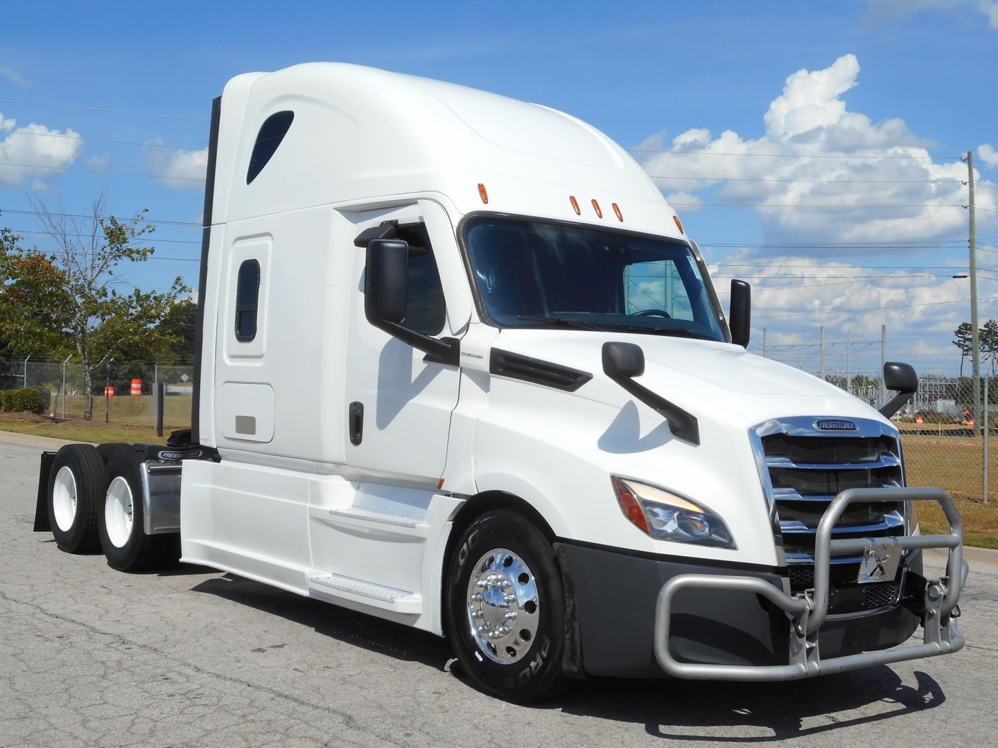 Truck cab of a white 2022 Freightliner Cascadia 126 sleeper tractor showing side view with chrome wheels and front grille guard.
