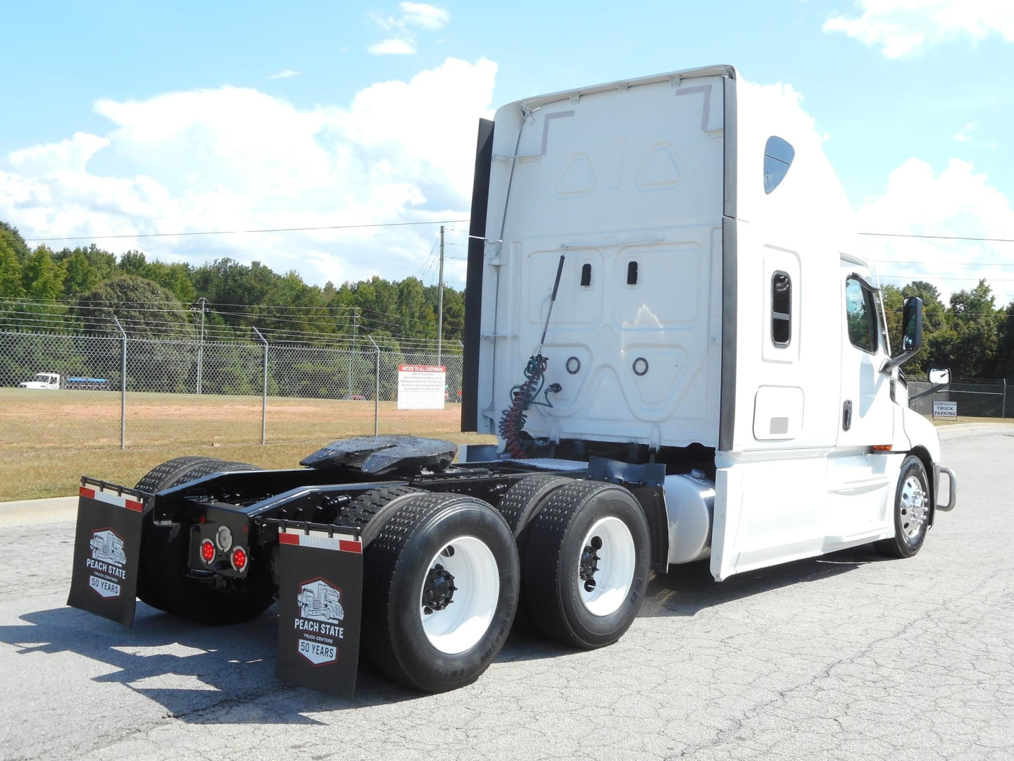 Truck chassis and cab of a white 2022 Freightliner Cascadia 126 semi-truck from rear quarter view showing drivetrain, dual rear axles, and sleeper cab.
