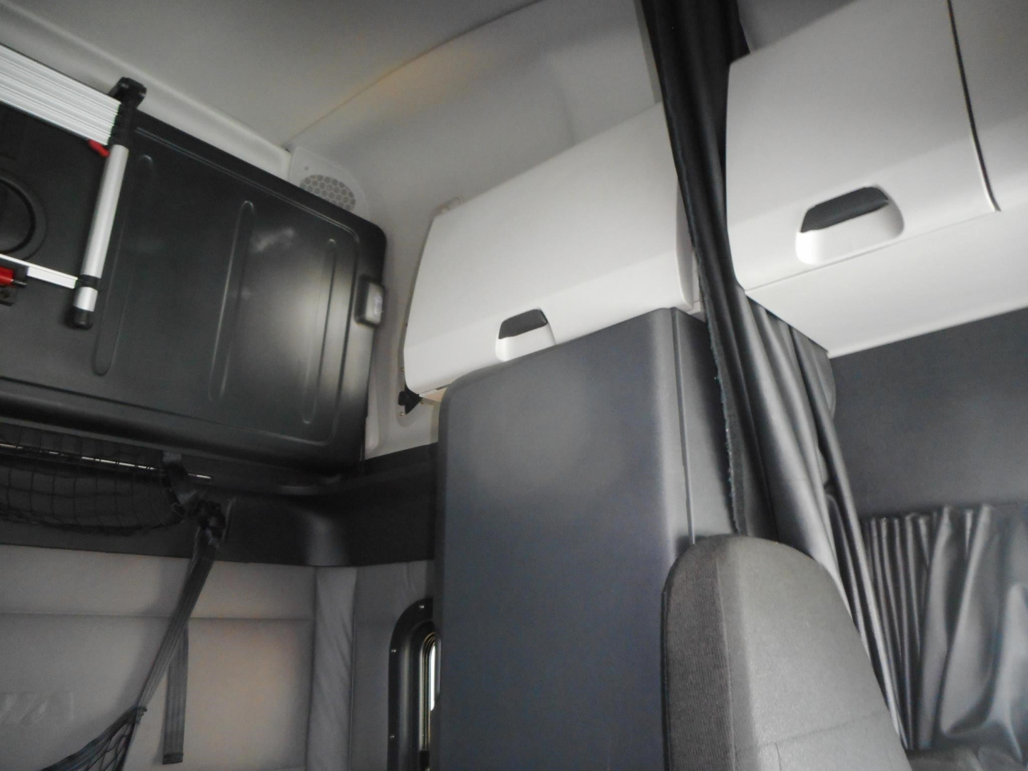 Cab interior of a Freightliner Cascadia showing overhead storage compartments and sleeper area.