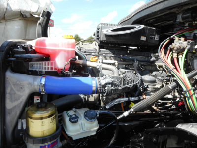 Freightliner Cascadia engine bay showing coolant reservoir, power steering cooler, and numerous hoses and wiring harnesses.