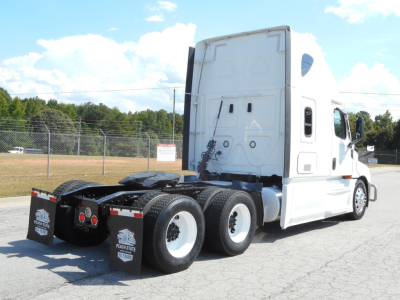 Truck chassis and cab of a white 2022 Freightliner Cascadia 126 semi-truck from rear quarter view showing drivetrain, dual rear axles, and sleeper cab.