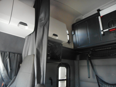 Freightliner Cascadia sleeper cab interior showing overhead storage and curtains with a mounted black toolbox and accessories.