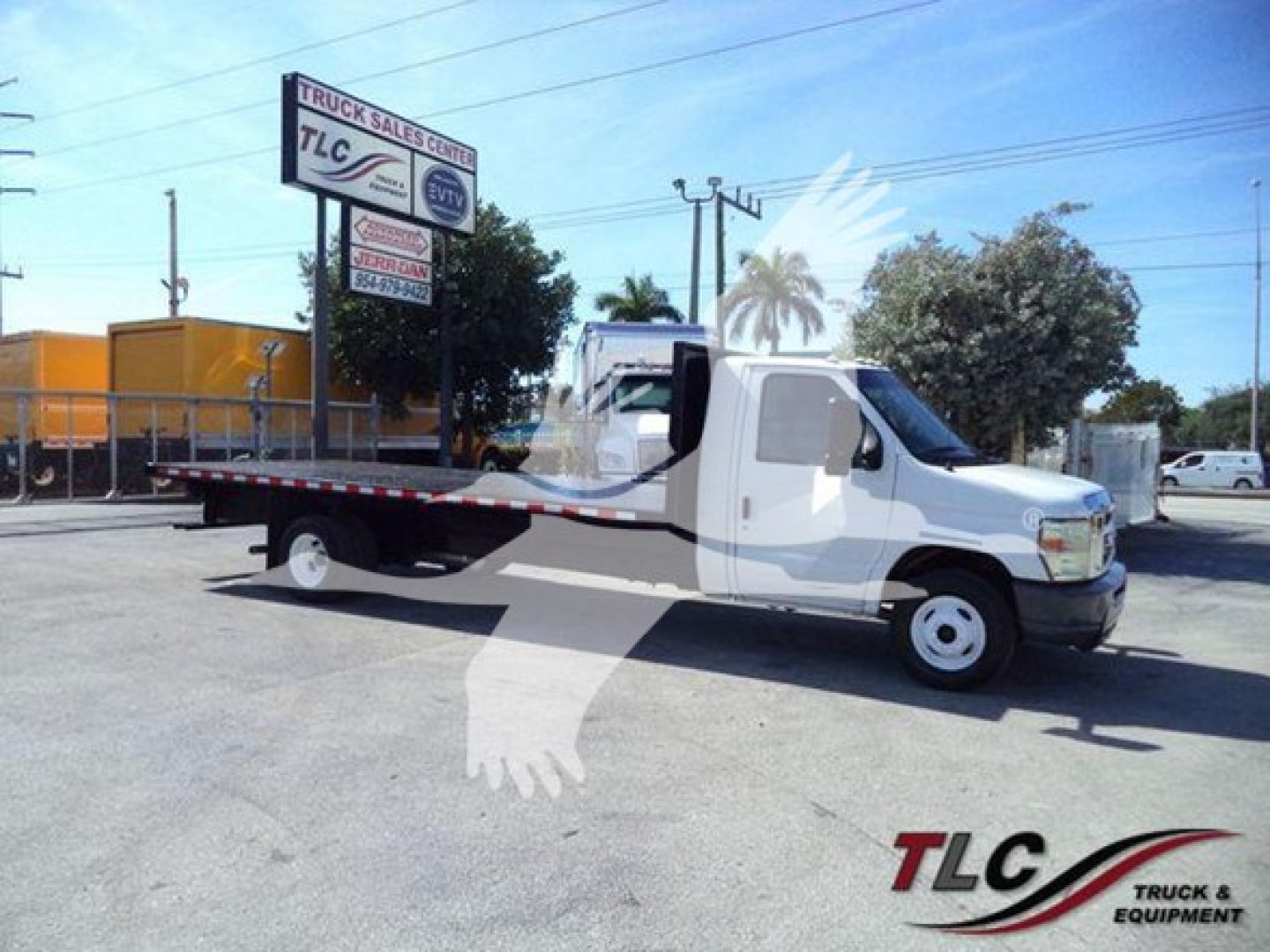 Flatbed tow truck showing long flatbed and white cab with Ford E-450 badge, VIN 1FDXE4FS9BDA22070 visible in listing, TLC Truck Sales Center sign in background.