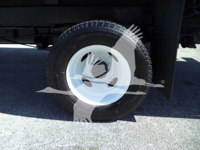 Ford E-450 flatbed truck wheel and tire close-up showing white steel rim and black tire undertruck frame.