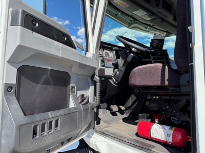  cab interior of a Mack MD7 truck showing driver seat, steering wheel, dashboard, and a fire extinguisher on the floor near the door opening.