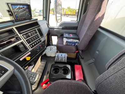 Cab interior of a Mack MD7 truck showing dashboard controls, center console with cup holders, and a mounted screen.