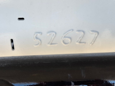 Vehicle identification number stamped on white metal with embossed digits 52627 near a black rail.