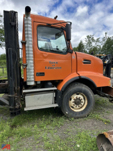 Orange 2004 Volvo VHD cab and chassis side view showing front wheel, cabin, exhaust stack, and Steps with Town of Edmeston text on door.