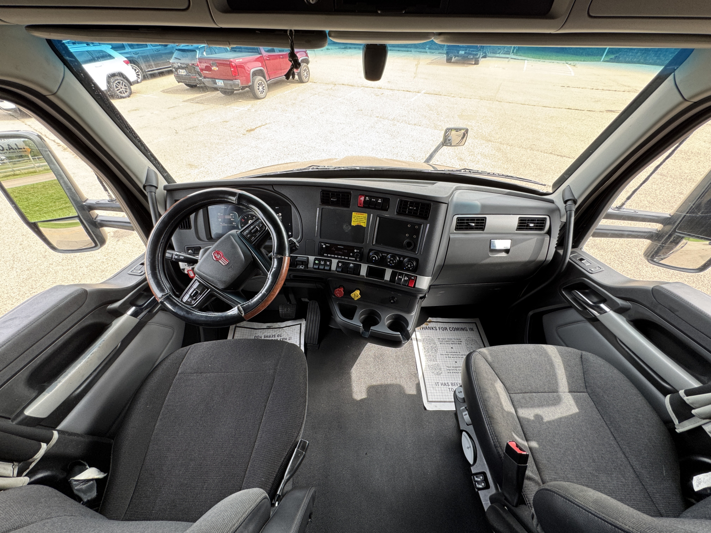 Kenworth T680 cab interior showing steering wheel, dashboard, and front seats from driver vantage point.