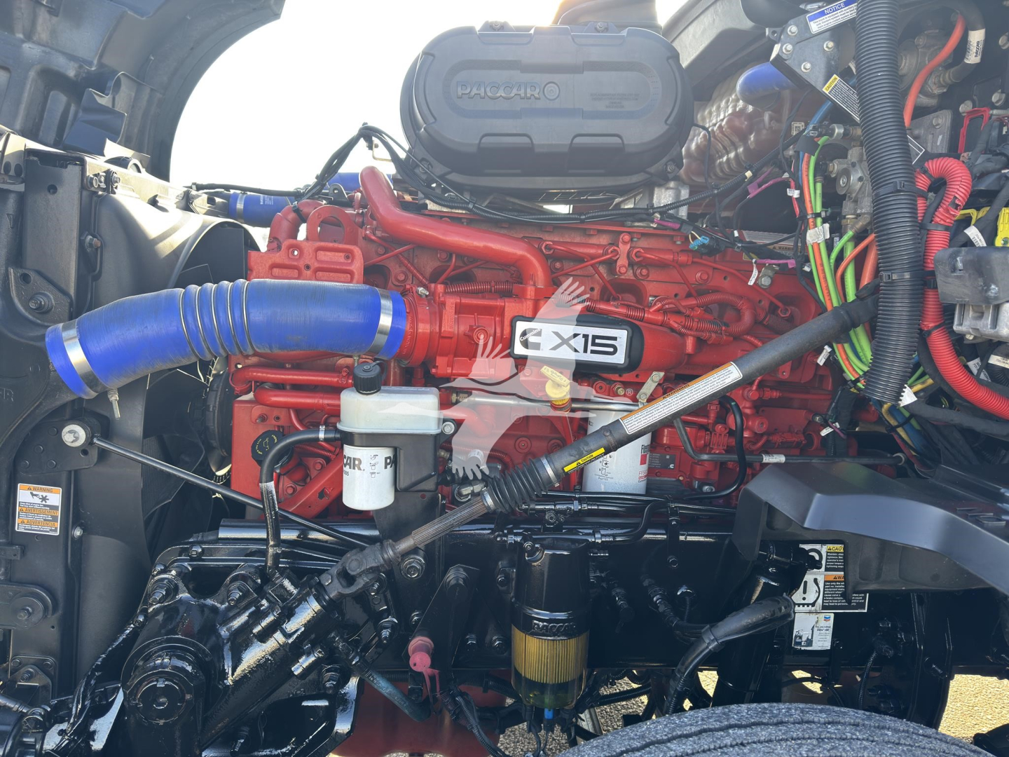 Kenworth T680 engine bay with red EXIS inline 6 engine, blue silicone intercooler hose, white reservoir, and various wiring harnesses visible.