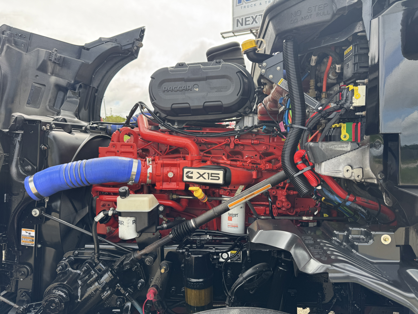 Kenworth T680 engine bay with red engine labeled X15, blue intercooler hose, various hoses and components visible.