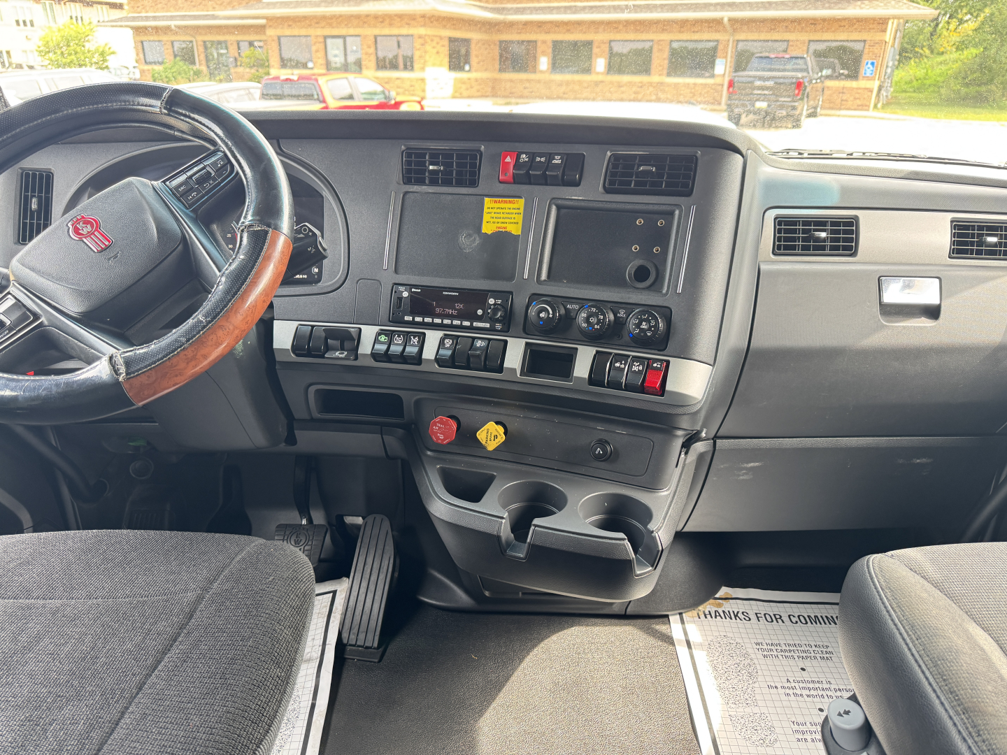 Kenworth T680 dashboard and steering wheel interior with center control panel, dual cup holders, and various switches visible.
