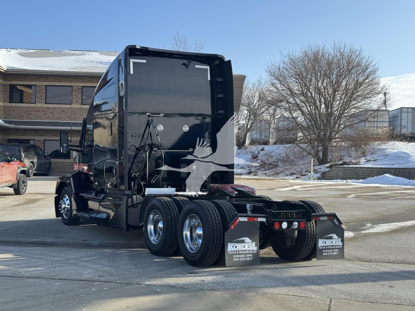 Kenworth T680 tractor rear view showing triple rear axles, black glossy exterior, mud flaps with Kordell dealer text, and winter scene.